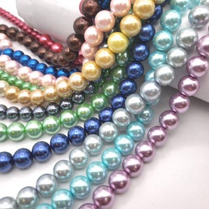 May include: A collection of beaded necklaces in various colors, including pink, brown, blue, green, yellow, and purple. The beads are round and have a glossy finish, suggesting they are made of glass or a similar material. The necklaces are arranged in a diagonal pattern.