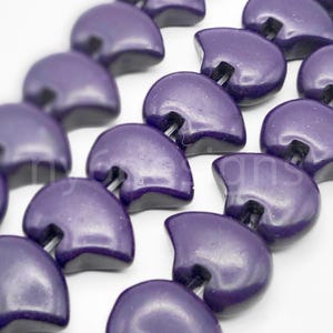 May include: A strand of purple, semi-circular beads with a glossy finish. The beads are strung on a wire and have a small hole in the center.