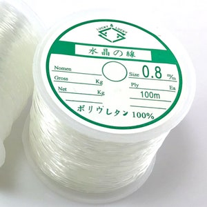 May include: A spool of clear elastic thread labeled "Lucky & Lucky 水晶の線" with the text "Size 0.8 m/m Ply 100m Ea" and "ボリウレタン 100%".