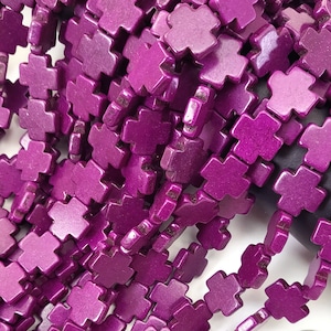 May include: A strand of purple cross-shaped beads. The beads are made of wood and have a matte finish.