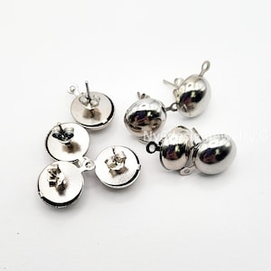 May include: A collection of silver-colored stud earrings. The earrings have a round, flat base with a post for insertion and a rounded, oval-shaped top. The earrings are displayed on a white surface.