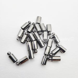 May include: A collection of silver-colored jewelry end caps and ball-end findings. The cylindrical end caps have a polished finish, and the ball ends are small and round. These components are used in jewelry making.