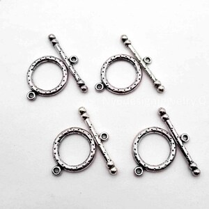 May include: Four silver-toned metal toggle clasps for jewelry making. Each set consists of a circular ring with a dotted texture and a matching T-bar component. The ring features a small loop at the bottom, and the T-bar has a small loop at the center.