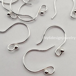 May include: Close-up of several silver-colored earring hooks with a small ball at the end of each hook. The hooks are arranged on a light gray surface. The text "Ny6designjewelry" is visible on the right side of the image.