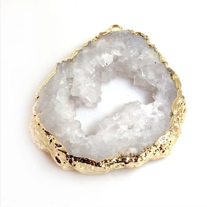 May include: A white geode pendant with a gold-colored, irregular edge. The geode has a hollow center and a rough, crystalline texture. The gold edge has a textured, metallic appearance. The pendant is designed for jewelry making.