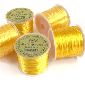May include: Four spools of yellow elastic thread, each with a label that reads "Polyurethane 100% Japanese Crystal Line" in Japanese and English.