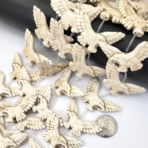 May include: A strand of white ceramic bird beads with intricate details. The beads are strung on a clear elastic cord and are approximately 1 inch in size.