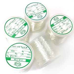 May include: Four spools of clear elastic thread, each with a green label that reads "Lucky Crystal Line Size 1.0m 50m Ply 100% Polyurethane".
