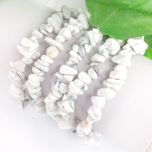 May include: Five white howlite chip bracelets stacked on top of each other. The bracelets are made of small, irregular shaped white stones with gray veining.