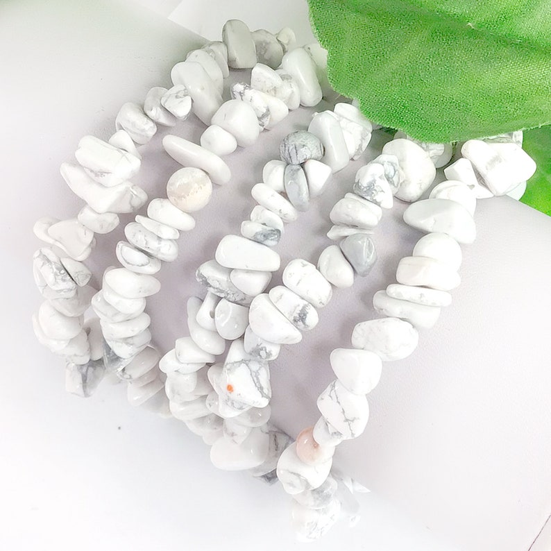 May include: Five white howlite chip bracelets stacked on top of each other. The bracelets are made of small, irregular shaped white stones with gray veining.
