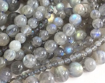 May include: A strand of iridescent gray labradorite gemstone beads. The beads are round and smooth, with a slight sheen. The beads are strung on a clear thread.