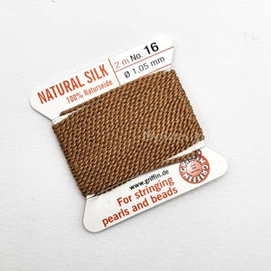 May include: A spool of brown natural silk thread for stringing pearls and beads. The label reads "NATURAL SILK" and "100% Naturseide". The thread is 2 meters long and 1.05 mm in diameter.