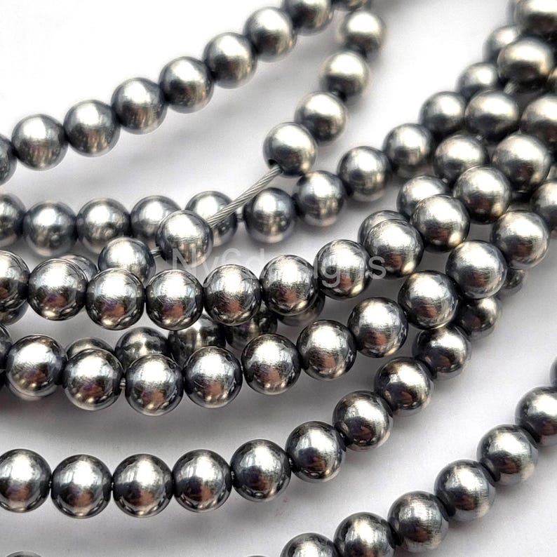 May include: Strands of gunmetal gray, round beads. The beads are smooth and reflective, strung together on a thin, silver-colored wire. The beads are approximately 8mm in diameter, perfect for jewelry making.
