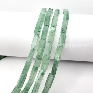 May include: Close-up of strands of green rectangular beads. The beads have a slightly translucent appearance with a speckled texture. The beads are strung together, creating a linear pattern. The background is white.