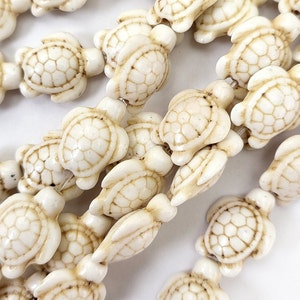 May include: A strand of white ceramic turtle beads. The beads are all the same size and shape, and they are strung together on a clear string.