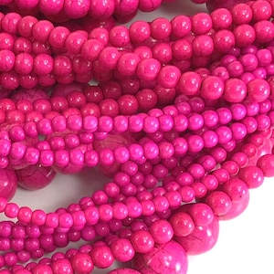 May include: A close-up of a strand of pink beads. The beads are round and have a smooth, polished finish. The beads are strung together on a clear thread.