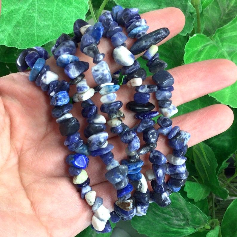 May include: A strand of blue and white gemstone chips, likely sodalite, strung on a cord. The chips are irregular in shape and size, and some have a white marbling.