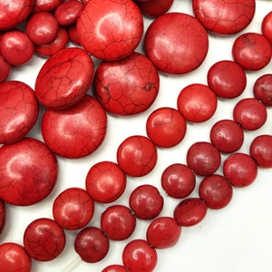 May include: A collection of red, round, smooth, and polished gemstone beads. The beads are of various sizes and are arranged in rows on a white surface.