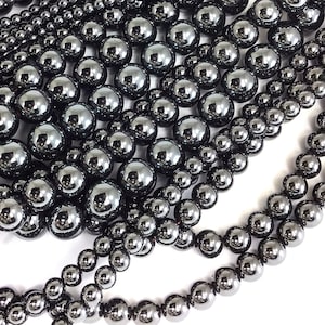 May include: A collection of black hematite beads in various sizes. The beads are smooth and shiny, with a metallic finish.