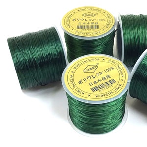 May include: Four spools of green elastic thread, each with a yellow label that reads "Polyurethane 100% Japanese Crystal Line" in Japanese characters. The label also includes a barcode and the date "20170713".
