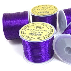 May include: Four spools of purple elastic thread, each with a yellow label that reads "Polyurethane 100% Japan Water Thread" and "Crystal Line".
