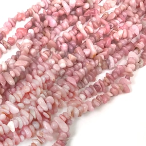 May include: A strand of pink gemstone chips, also known as pink opal, arranged in a loose pile. The chips are irregular in shape and size, with a smooth, polished finish.