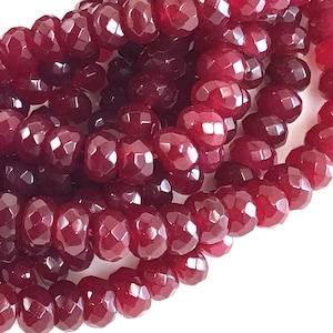 May include: A strand of deep red faceted gemstone beads. The beads are round and have a smooth, polished finish.
