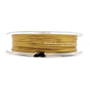 May include: A spool of gold-colored beading wire. The wire is tightly wound on a clear plastic spool. The spool is set against a white background. The wire appears to be fine and flexible, suitable for jewelry making.