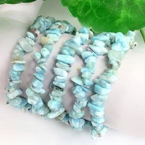 May include: A set of four turquoise blue gemstone chip bracelets. The bracelets are made of small, irregular shaped chips of turquoise blue gemstone. The bracelets are stacked on top of each other.