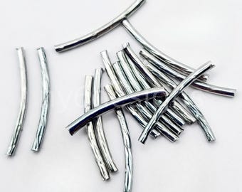 May include: A pile of silver metal tube beads. The beads are approximately 2.5 cm long and have a slightly curved shape.