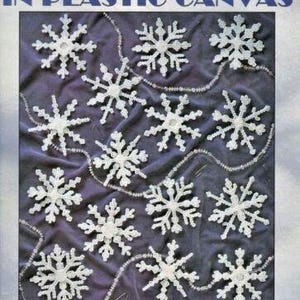 May include: A craft pattern booklet for making snowflakes out of plastic canvas. The cover features a white background with a string of white snowflakes. The title of the booklet is "Snowflakes in Plastic Canvas" and the text "Create Your Own Snowflakes with Interchangeable Patterns" is printed below the snowflakes. The author's name, "By Joan Green", is printed at the bottom of the cover.