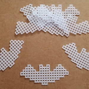 May include: A set of white plastic bat shapes with a grid pattern. The bats are arranged in a circle on a brown surface.