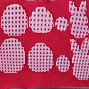 May include: Eight white plastic canvas shapes, including circles and bunnies, on a red felt background. The shapes are all the same size and have a grid pattern.
