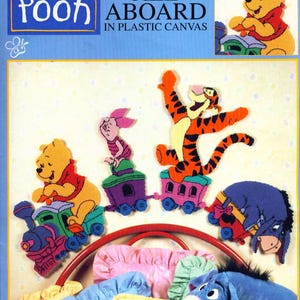 Puede incluir: Un kit de manualidades con Winnie the Pooh y sus amigos. La imagen muestra a Pooh, Piglet, Tigger y Eeyore en un tren, con el texto "Pooh All Aboard in Plastic Canvas". El kit incluye un marco de cama y almohadas.