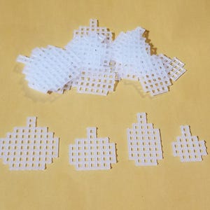 May include: A set of white plastic mesh squares, perfect for crafting projects. The squares are various sizes and are arranged in a pile on a beige surface.