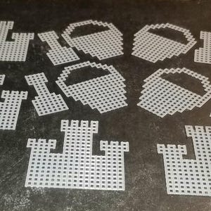 May include: A set of ten white plastic craft shapes, including castles and buckets. The shapes are designed for use with plastic canvas.