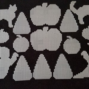 May include: A set of 16 white plastic shapes for crafting, including pumpkins, ghosts, cats, and triangles. The shapes are designed for cross-stitch or other needlework projects.