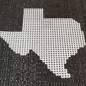 May include: White plastic canvas shaped like the state of Texas. The canvas is made up of small squares, perfect for cross-stitch or other needlework projects.