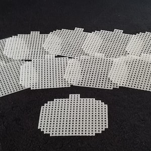 May include: A set of ten white plastic canvas sheets, each with a grid pattern. The sheets are arranged in a fan shape, with one sheet in the center and the others radiating out from it.