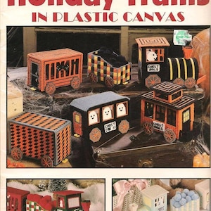 May include: A craft leaflet cover featuring various plastic canvas holiday train designs. The trains are in orange, black, and green, with Halloween and Christmas themes. The text "Holiday Trains in Plastic Canvas" is displayed.