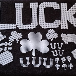 May include: White plastic craft pieces spelling out the word "LUCK" with various other lucky charms including shamrocks, horseshoes, and a top hat.