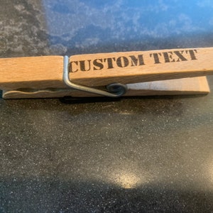 May include: A wooden clothespin with a metal spring and the text "CUSTOM TEXT" engraved on the top.