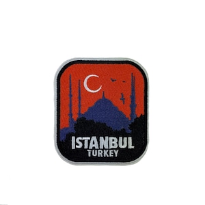 May include: A rectangular embroidered patch with rounded corners featuring a dark blue silhouette of a mosque with minarets against an orange sky. A white crescent moon and birds are visible above the mosque. The text ISTANBUL TURKEY is in white.