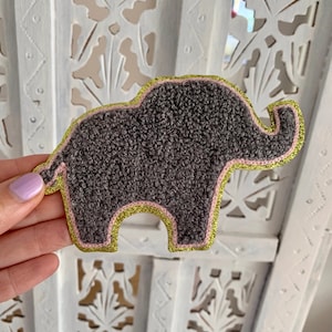 May include: A grey felt elephant applique with pink and gold stitching. The applique is ideal for adding a touch of whimsy to any project.