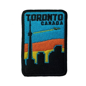 May include: Embroidered patch with a black outline and a blue background. The patch features a silhouette of the Toronto skyline with the CN Tower and the text "Toronto Canada".