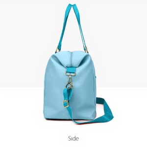 May include: A light blue duffel bag featuring a zipped top closure, two long shoulder straps, and a detachable, adjustable crossbody strap. The bag includes gold-toned metal hardware clips and buckles, with a smooth, solid-coloured exterior finish.