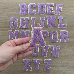 May include: A set of 26 purple felt letters with gold glitter trim. The letters are in uppercase and are arranged in alphabetical order. The letter A is being held in a hand.