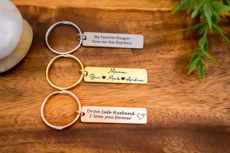 K&ouml;nnte beinhalten: Drei silberne Schl&uuml;sselanh&auml;nger mit gravierten Botschaften. Der obere Schl&uuml;sselanh&auml;nger lautet "My Favorite Daughter Gave me this Keychain". Der mittlere Schl&uuml;sselanh&auml;nger lautet "Mama Ben Mark Andrea". Der untere Schl&uuml;sselanh&auml;nger lautet "Drive Safe Husband I love you forever".
