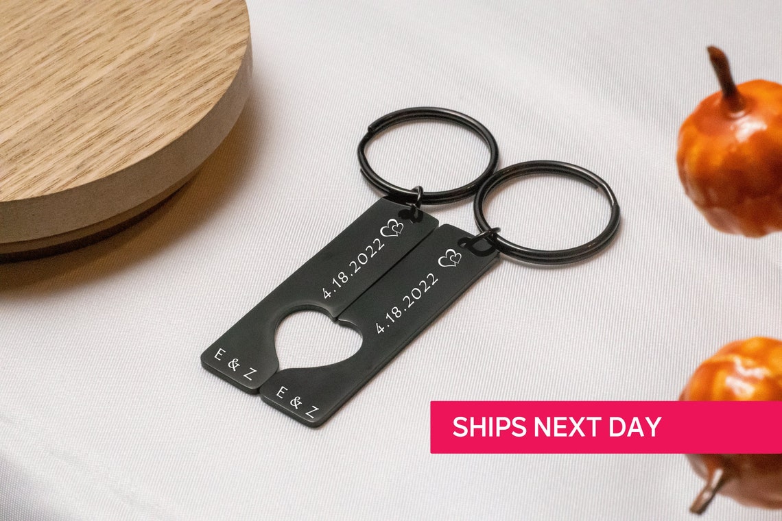 May include: Two black metal keychains with interlocking heart cutouts. The keychains are engraved with the initials "E & Z" and the date "4.18.2022".