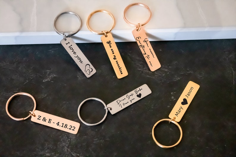 K&ouml;nnte beinhalten: Ein Set aus sechs Schl&uuml;sselanh&auml;ngern in Silber und Gold mit gravierten Botschaften. Die Botschaften lauten: "Ich liebe dich", "Du bist mein Sonnenschein", "Alles f&uuml;r mich", "Fahr vorsichtig mein Schatz ich liebe dich", "Z & E - 4.18.22" und "Mary Jason".